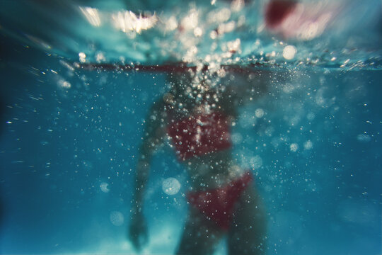 A girl jumps into a swimming pool making lots of bubbles - Powered by Adobe