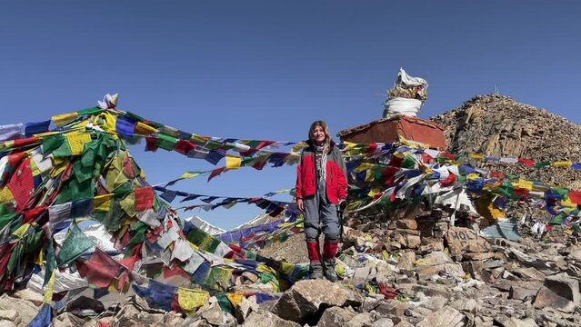 Young woman traveler standing on a high pass in the Himalayan mountains under Buddhist Tibetan prayer  flags overlooking the mountain peaks