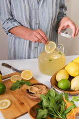 Woman's hands preparing homemade lemonade.  lime, lemon, mint on the kitchen table.