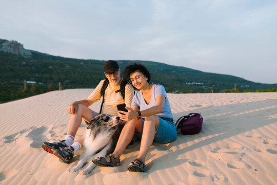 Happy middle-age couple with their dog using cell phone