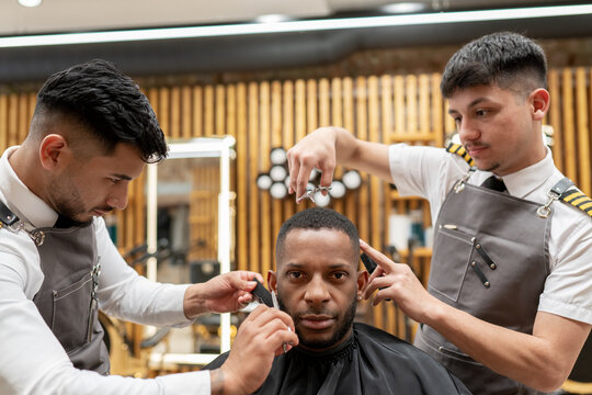 Close Up Of Two Barbers Working With One Client