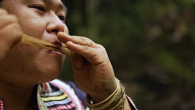 close up shot of an Indigenous person playing Kubing tribal instrument, behind is a waterfall
