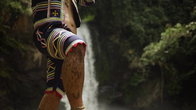 Indigenous person playing Kubing tribal instrument, behind is a waterfall while standing