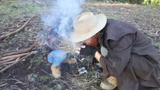 A bushman in a stockman jacket creates fire from a spark with his son.