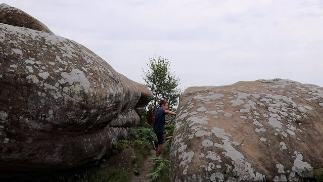 Young boy climbing and jumping on the rocks at Brimham Rocks, once known as Brimham Crags in North Yorkshire, surrounded by woodland in the UK.