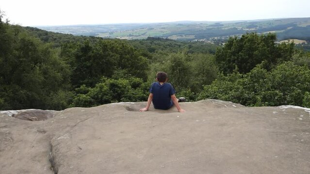 Young boy looking out across the countryside at Brimham Rocks, once known as Brimham Crags in North Yorkshire, surrounded by woodland in the UK.