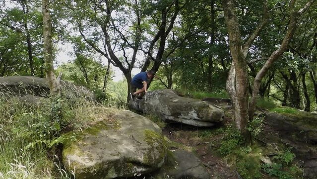 Young boy climbing and jumping on the rocks at Brimham Rocks, once known as Brimham Crags in North Yorkshire, surrounded by woodland in the UK.