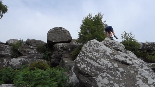 Young boy climbing and jumping on the rocks at Brimham Rocks, once known as Brimham Crags in North Yorkshire, surrounded by woodland in the UK.