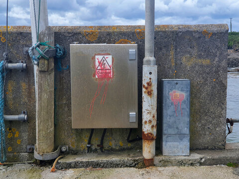 An electricity supply box on a harbour wall with danger signs