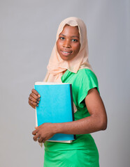 An African Muslim lady, female student or businesswoman with head scarf called hijab, holding a...