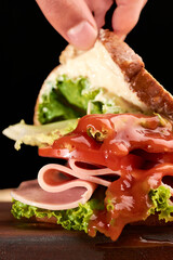 Sandwich prepared with Italian lettuce, ham, tomato slices, bacon and mayonnaise, a splash of tomato sauce is added, the bread is lifted from one side with the fingers
