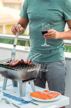 Young Man Cooking On Grill And Drinking Wine On Terrace