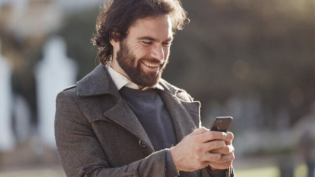 Excited man texting on a phone outside on a cold morning. Attractive casual male looking happy and cheerful checking social media while standing alone. Trendy young guy writing and replying to emails