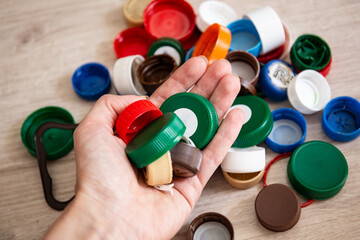A hand holds colored plastic bottle caps. Sorting of garbage and waste. Plastic lids from HDPE for...