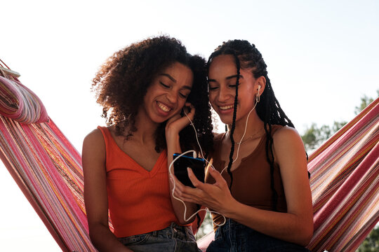 Happy friends sharing music with earphones in hammock