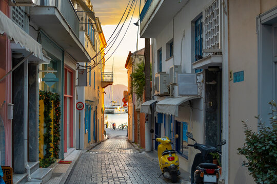 Fototapeta Boats in the port harbor at sunset viewed from a narrow alley of shops and homes on the Greek island of Aegina, Greece, one of the picturesque Saronic Islands near Athens.