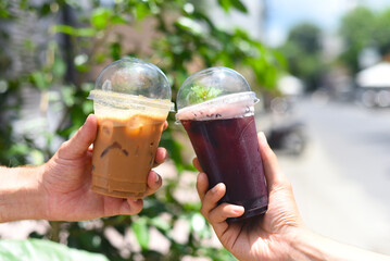 Hand holding plastic cups of coffee and mulberry tea closeup 