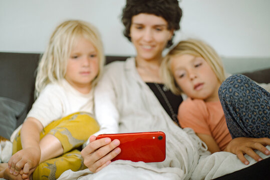 Two boys and an adult woman are watching cartoons on a smartphone. 