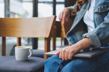 Fototapeta premium Closeup image a woman holding and putting laptop computer on her lap with coffee cup on a chair
