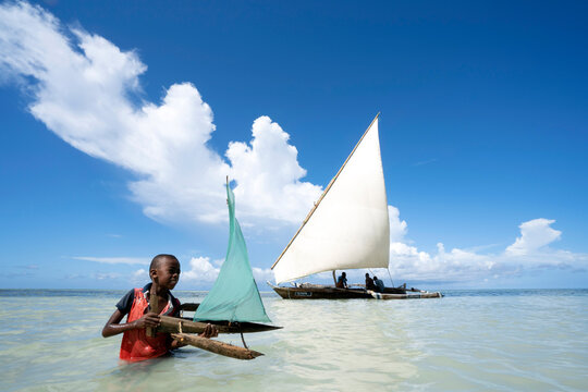 Boy playing with toy boat, traditional dhow in the background. 