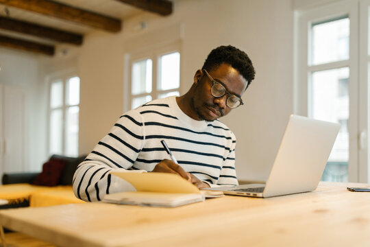 Young man taking notes in notebook from online meeting