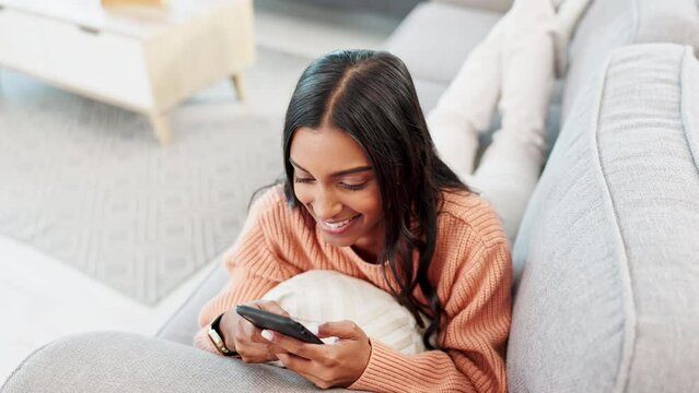 Happy girl texting on her phone while taking a break at home. One smiling young woman reading messages online and checking her social media apps on a relaxing afternoon inside her modern apartment