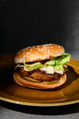 Classic american burger on ceramic plate in dark minimal style. Beef burger on gray stone table with hard shadow. Fast food dark concept. American burger on gray concrete background. Simple food menu.