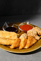Platter appetizers with fried cheese, chiken wings, nuggets and sauces. Fried appetizers on gray stone background. Fast food on plate on concrete background with shadow. Tempura set - cheese sticks.