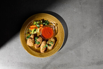 American appetizers buffalo wings with vegetables and sauce on gray stone table. Beer appetizer - Bbq wings on concrete background with hard shadow. Dark menu for pub. Chicken wings. Junk food.
