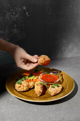 American appetizers buffalo wings with vegetables and sauce on gray stone table. Bbq wings in woman hand on concrete background with hard shadow. Female hand holding chicken wings. Junk food.