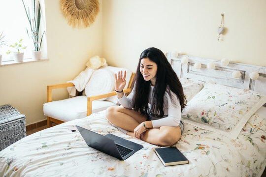 Young woman sitting on bed making video call with laptop