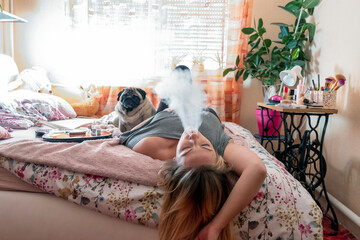 Woman relaxing with a dog in bed and smoke