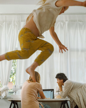 A young boy jumps against the background of his mother in room