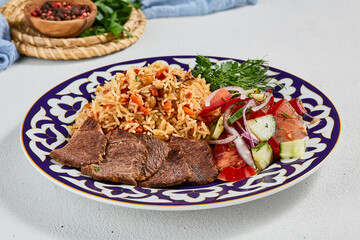 Traditional uzbek food - plov with beef. Eastern cuisine - pilaf with rice, meat and spices. Plov with beef on traditional uzbek plate. Composition of oriental ceramic plate with pilaf.