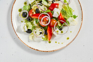 Classic greek salad with pesto sauce on ceramic plate. Vegetable salad with tomatoes, cucumber, paprika, onion and olives. Traditional grecian food. Greek salad on concrete background.