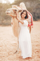 Fototapeta na wymiar Portrait of asian young woman tourist in white dress and landscape with tourists riding on camels is popular travel destination in Mui Ne desert, Vietnam
