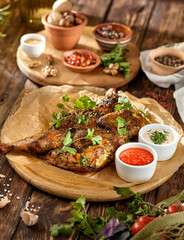 Traditional georgian dish - chicken tabaka on wooden background in rustic style. Roasted whole chicken in georgian style on wooden table. Chicken tabaka with sauces in rustic style.