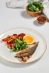 Fish dish - roasted dorado fillet with vegetables. Grilled fish fillet and roasted paprika, tomatoes and onion. Roast dorado fillet with garnish, greens and lemon on ceramic plate.