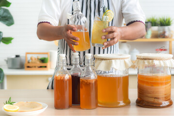 Chef's hand holds a bottle and a glass of Homemade fermented kombucha tea, variety of flavors in...
