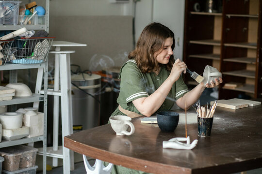 Young woman cleans a clay mug from excess clay dust