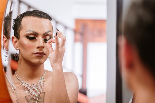 Trans man removing his eyelashes in front of the mirror