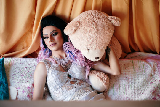 Drag queen lying on a bed hugging a stuffed animal