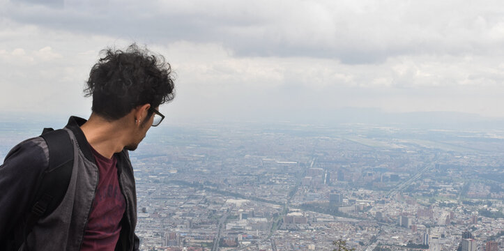Joven con gafas en la cima de una monta&ntilde;a y la ciudad de fondo