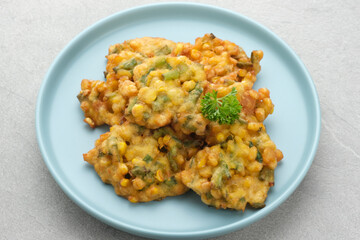 Perkedel Jagung or Bakwan Jagung, corn fritters is Indonesian traditional food. Savoury snack made of corn, egg, flour, spring onion, pepper and salt. Served in plate on grey background.
