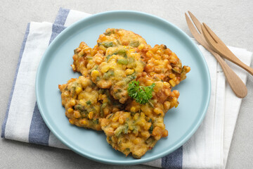 Perkedel Jagung or Bakwan Jagung, corn fritters is Indonesian traditional food. Savoury snack made of corn, egg, flour, spring onion, pepper and salt. Served in plate on grey background.
