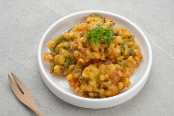 Perkedel Jagung or Bakwan Jagung, corn fritters is Indonesian traditional food. Savoury snack made of corn, egg, flour, spring onion, pepper and salt. Served in plate on grey background.

