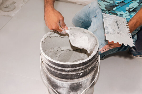 Unrecognizable ceramic tile installer taking glue from a bucket
