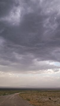 Timelapse of dark storm clouds moving over desert landscape looking down dirt road in Utah.