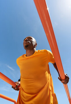Determined black guy exercising on metal bars on street