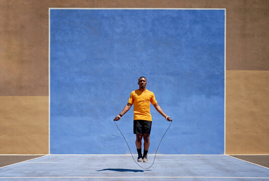 Fit black sprinter jumping in stadium on sunny day
